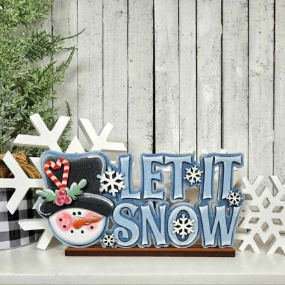 Decorative sign with 'Let It Snow' text and snowman design on a wooden background
