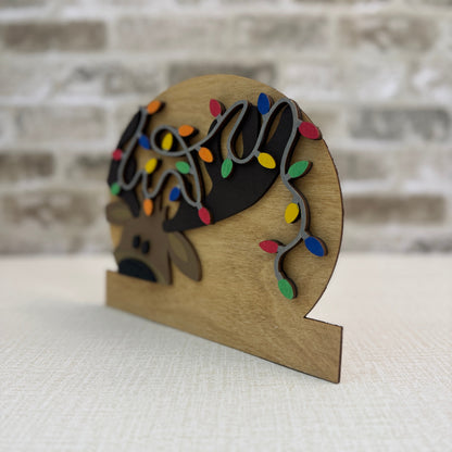 Wooden ornament with a reindeer and Christmas lights against a brick wall background