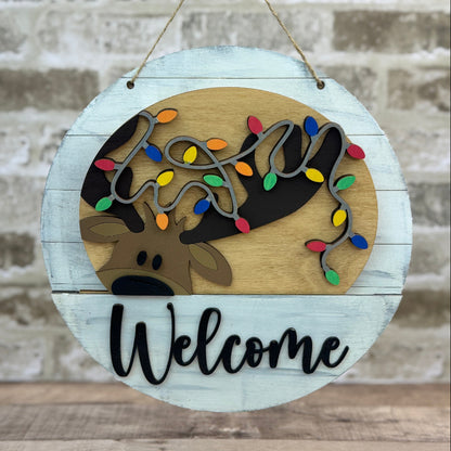 Round wooden sign with reindeer design and 'Welcome' text, hanging against a textured wall.