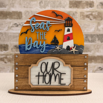 Decorative sign with lighthouse and text 'Seas the Day, Our Home' 
