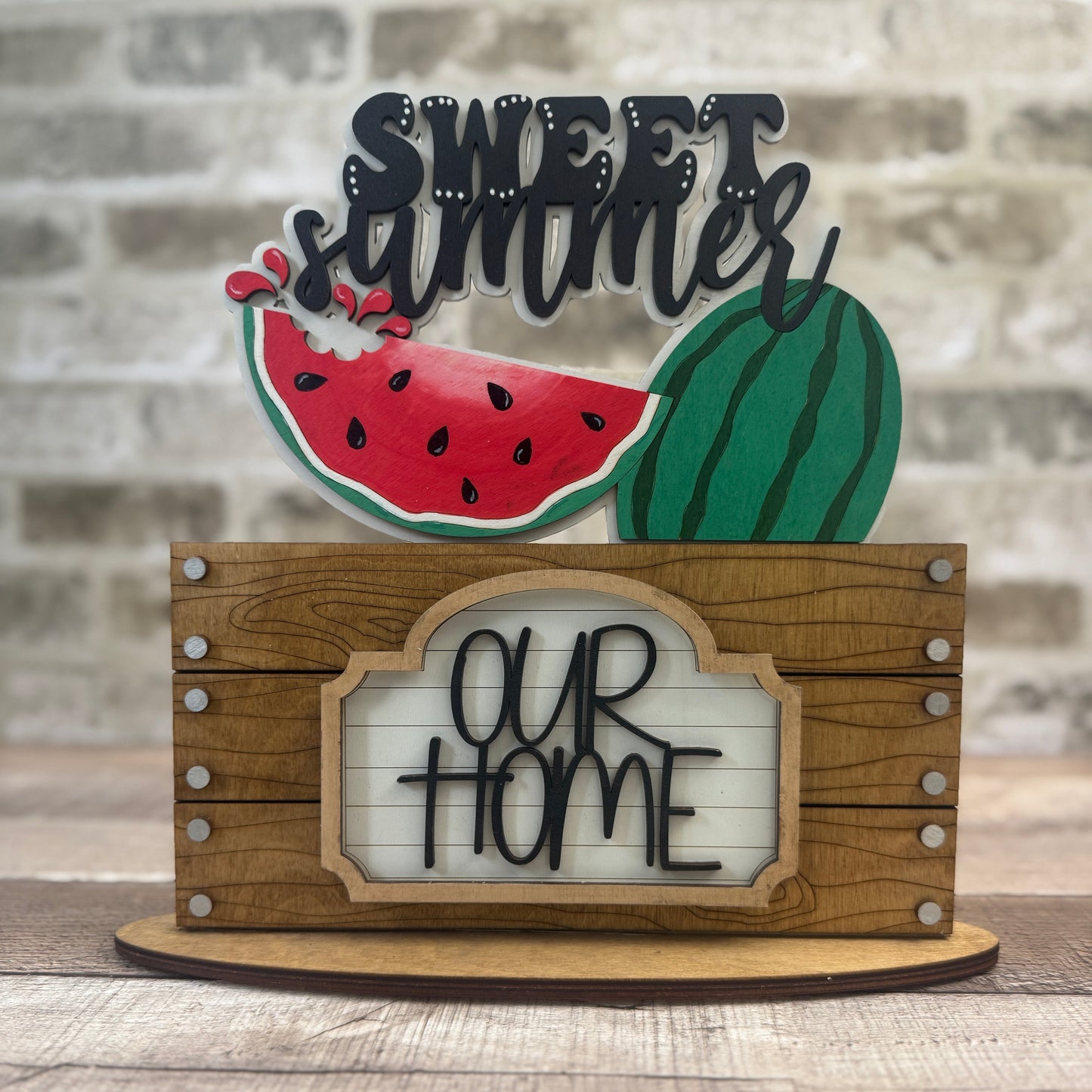 Decorative sign with watermelon design and text 'Sweet Summer Our Home' on a wooden stand.