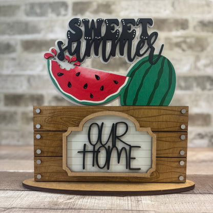 Decorative sign with watermelon design and text 'Sweet Summer Our Home' on a wooden stand.