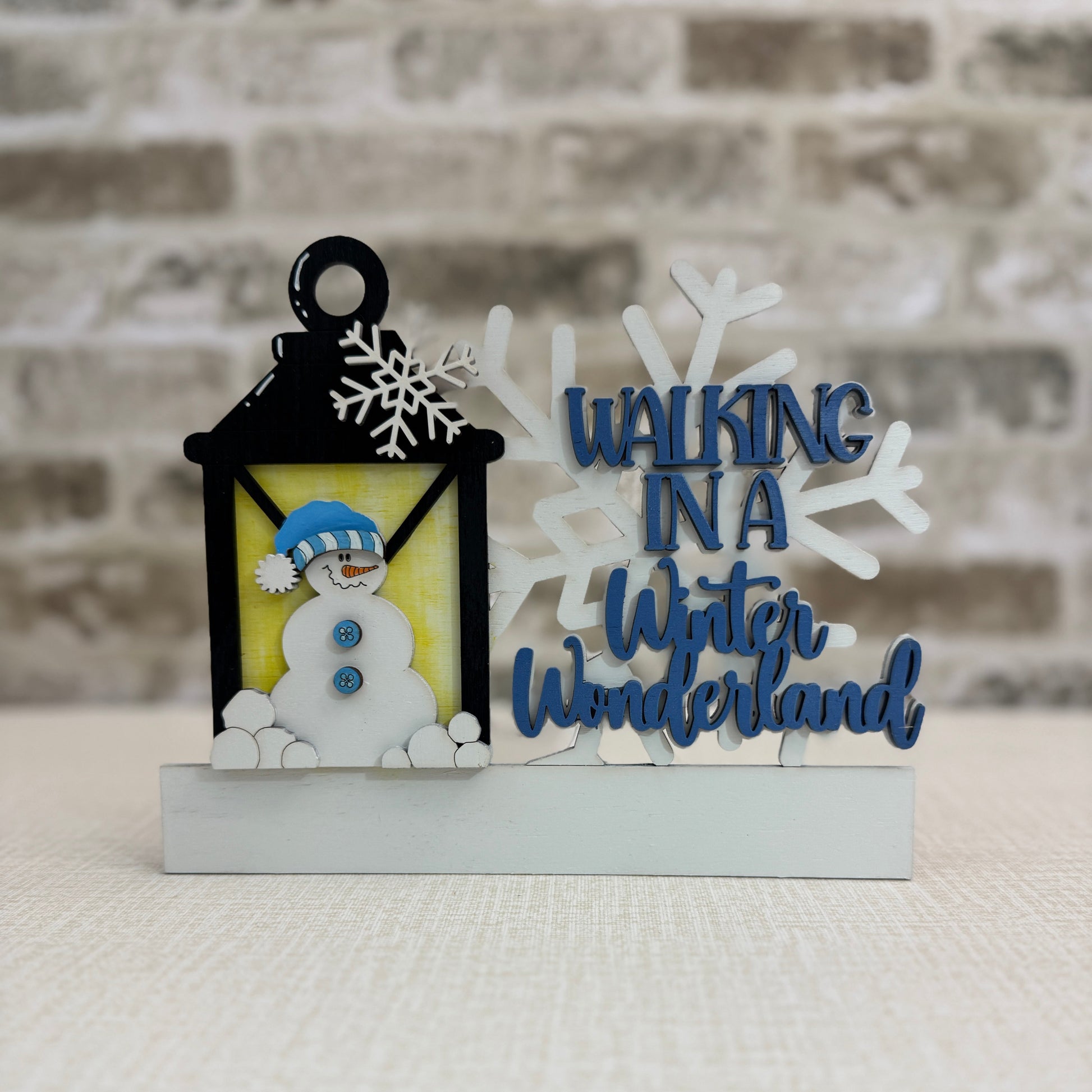 Decorative item with a snowman in a lantern and 'Walking in a Winter Wonderland' text against a brick wall.